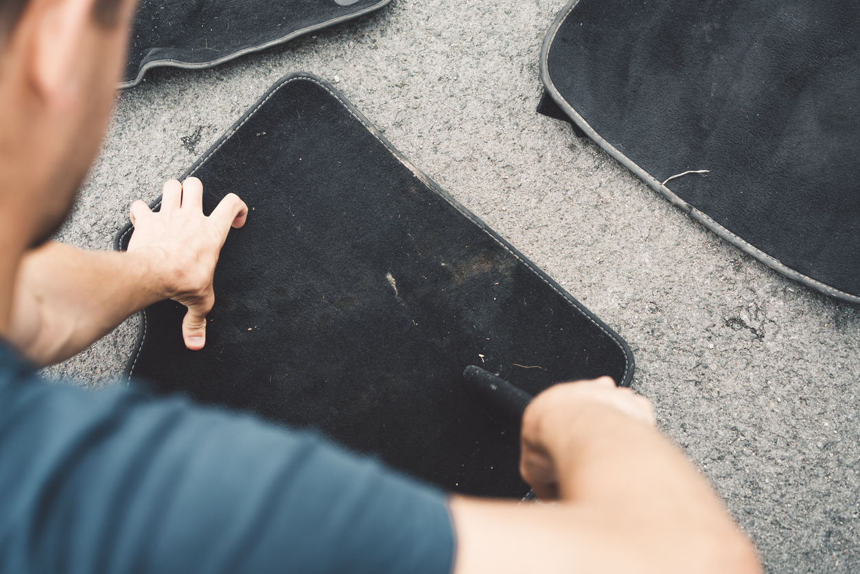 Man is exhaustively cleaning car mats outdoors