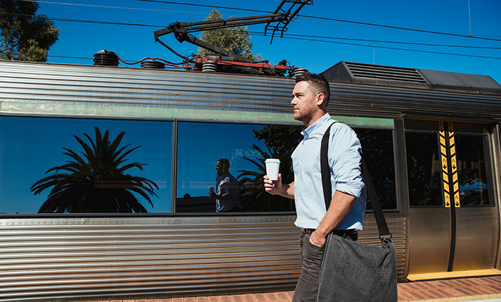 Photo of a man with a coffee walking on a train platform next to a train