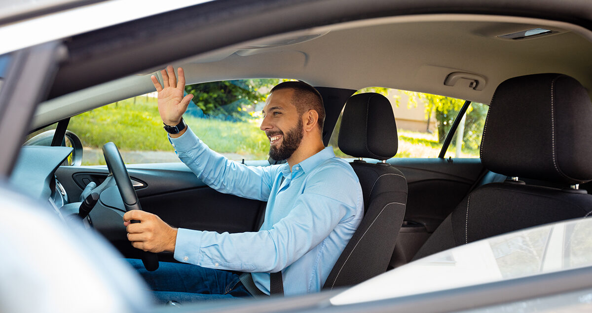 Young man happily driving a car and waving - being courteous