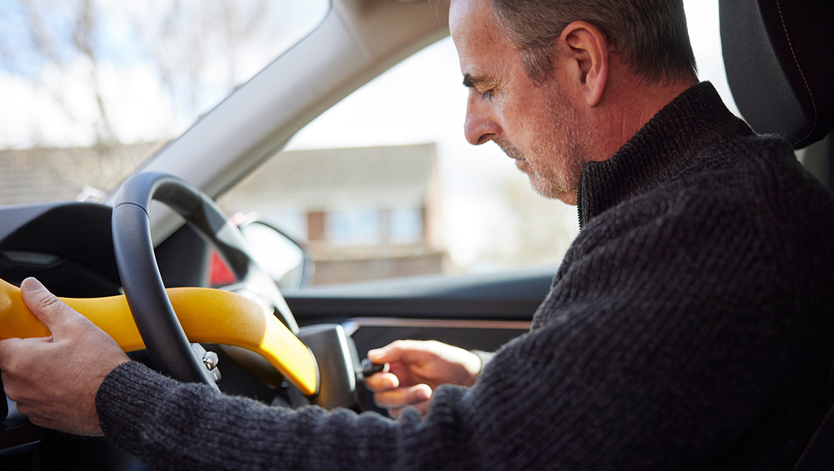 Person using a steering wheel lock in their car to protect it from theft