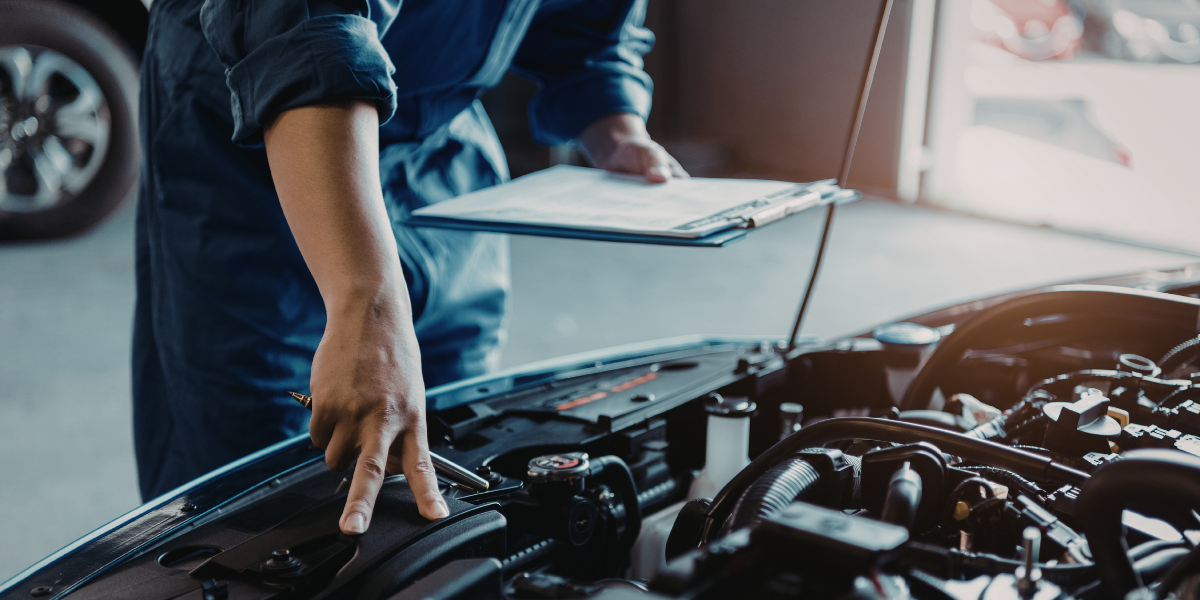 Mechanic assessing a vehicle's engine with the bonnet open, holding a clipboard